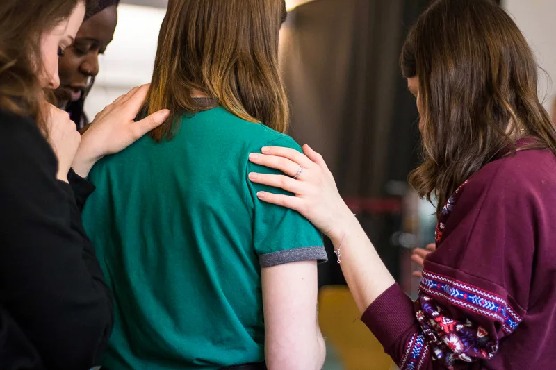 women gathered around a friend to pray for her